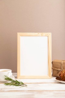 White wooden frame mockup with cup of coffee and cake on brown background. Blank, side view, still