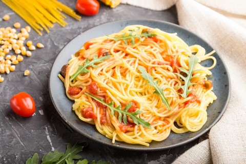 Corn noodles with tomato sauce and arugula on a black concrete background and linen textile. Side