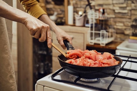 Unrecognizable man stirring chopped chicken fillet in frying pan with wooden spatula