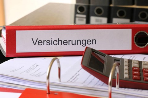 Symbolic image: Folder with insurance policies and calculator on a desk