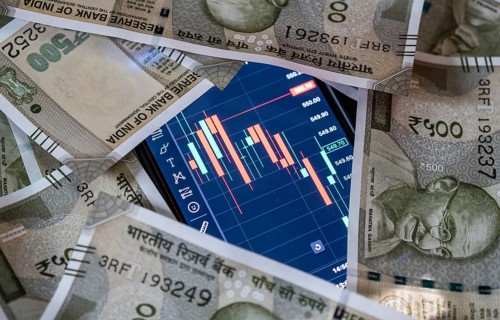 Stock market graph or chart display on a mobile phone against Indian 500 rupee paper currency note