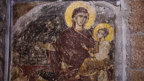 A detail of a medieval fresco showing a saint with a halo holding a child against a weathered