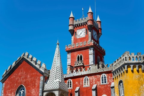 Red tower with clock and architectural decorations under a blue sky, detail, Palácio Nacional da