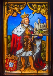 Depiction of a king with crown and mantle in front of a castle, in a medieval stained glass window,