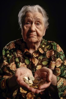 An elderly woman holds coins in both hands and looks sadly into the camera, symbolising poverty in