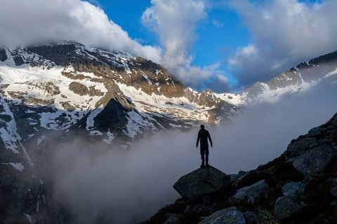 Silhouette of a mountaineer in front of a cloudy, atmospheric mountain landscape, rocky