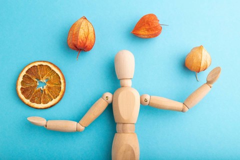 Wooden mannequin juggling dried citrus and physalis on blue pastel background. close up, isolated