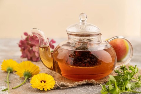 Red tea with herbs in glass teapot on brown concrete background and linen textile. Healthy drink