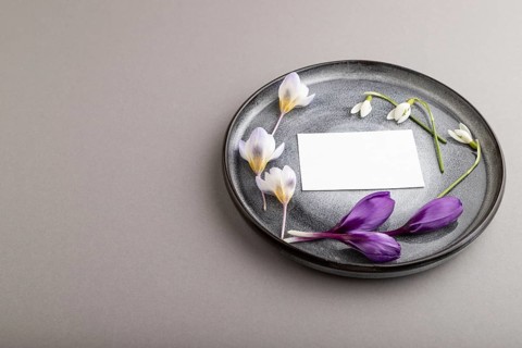 White paper invitation card, mockup with crocus and galanthus flowers on ceramic plate and gray