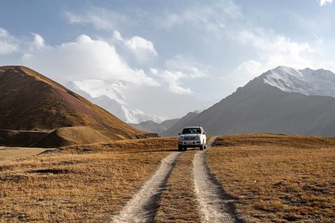 Off-road vehicle on a track between yellow meadows, glaciated high mountain peaks in the