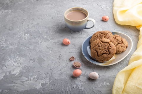 Homemade oatmeal cookies with a cup of cocoa and a yellow textile on a gray concrete background.