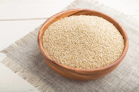 Wooden bowl with raw white quinoa seeds on a white wooden background and linen textile. Side view,