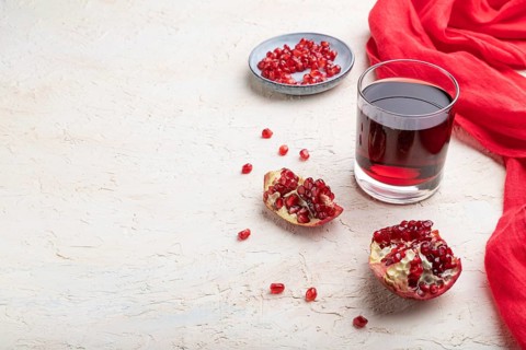 Glass of pomegranate juice on a white concrete background with red textile. Side view, copy space,