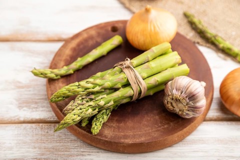 Bunch of fresh green asparagus, garlic, onion on white wooden background. Side view, selective