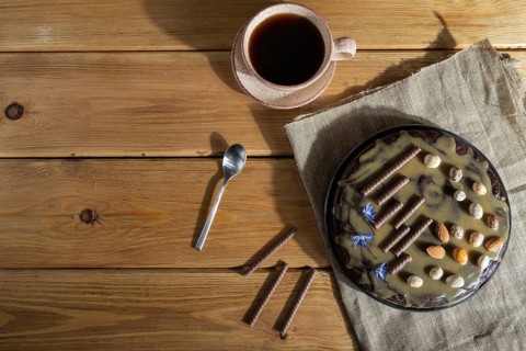 Homemade chocolate brownie cake with caramel cream and almonds with cup of coffee on wooden