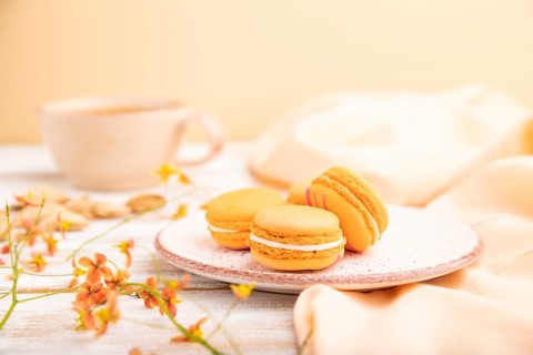 Orange macarons or macaroons cakes with cup of apricot juice on a white wooden background and