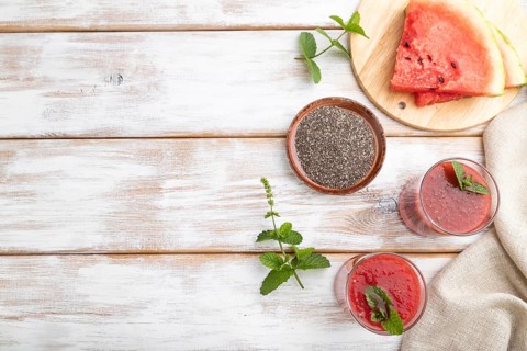 Watermelon juice with chia seeds and mint in glass on a white wooden background with linen textile.