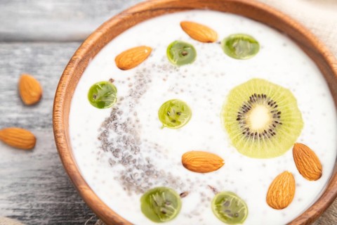Yogurt with kiwi, gooseberry, chia and almonds in wooden bowl on gray wooden background and linen