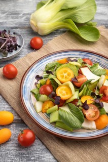 Vegetarian salad of pac choi cabbage, kiwi, tomatoes, kumquat, microgreen sprouts on gray wooden