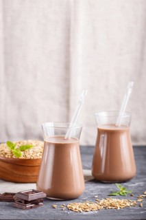 Organic non dairy oats chocolate milk in glass and wooden plate with oats seeds on a black concrete