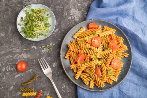 Tortiglioni semolina pasta with tomato and microgreen sprouts on a black concrete background and