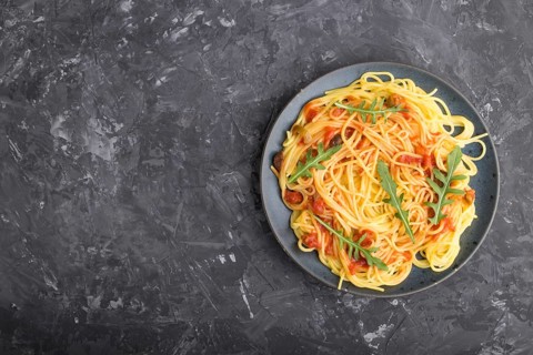 Corn noodles with tomato sauce and arugula on a black concrete background. Top view, flat lay, copy
