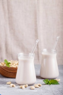 Organic non dairy cashew milk in glass and wooden plate with cashew nuts on a gray concrete
