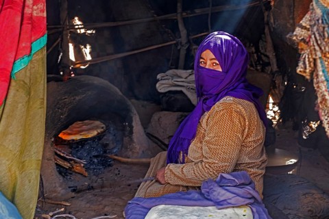 Nomadic Bedouin woman with hijab baking bread in traditional oven in tent in the Sahara Desert near