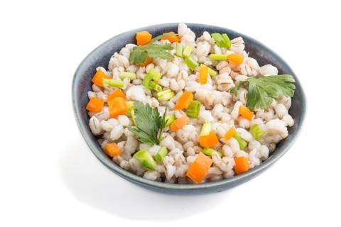 Pearl barley porridge with vegetables in blue ceramic bowl isolated on white background. Side view,