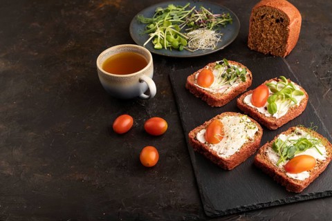 Red beet bread sandwiches with cream cheese, tomatoes and microgreen on black concrete background.