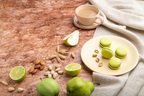 Green macarons or macaroons cakes with cup of coffee on a brown concrete background and linen