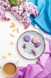 Purple macarons or macaroons cakes with cup of coffee on a white concrete background and