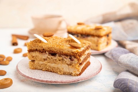 Honey cake with milk cream, caramel, almonds and a cup of coffee on a white concrete background and