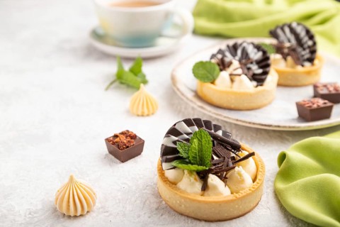 Sweet tartlets with chocolate and cheese cream with cup of coffee on a gray concrete background and