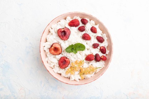 Rice flakes porridge with milk and strawberry in ceramic bowl on white concrete background. Top