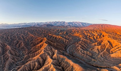 Riverbed in a landscape of eroded hills, badlands at sunrise, Issyk Kul Lake in the background,