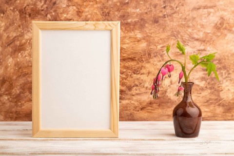 Wooden frame with pink dicentra, broken heart in ceramic vase on brown concrete background. side