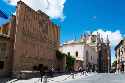 Pedestrian zone in Toledo with historic buildings and a Gothic church under a blue sky, art school,