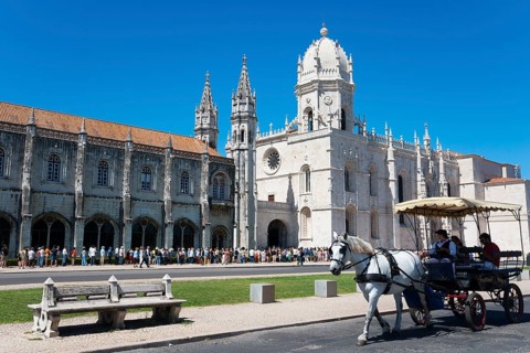 Eine gotische Kathedrale unter klarem blauen Himmel mit Touristen und einer Kutsche mit Pferden im