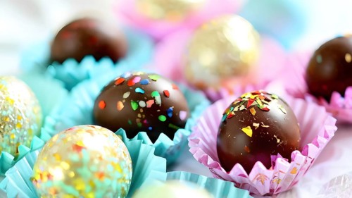 Small chocolate Easter eggs wrapped in shiny foil, placed on a bed of shredded pastel-colored