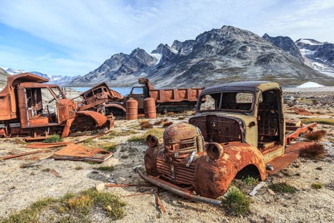 Rusty cars and oil drums in front of steep mountains, remains of a US airbase from the Second World