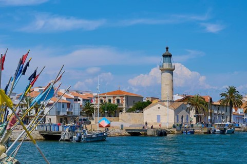 Coastal town with colourful houses and palm trees, boats in the water and a lighthouse, on a sunny