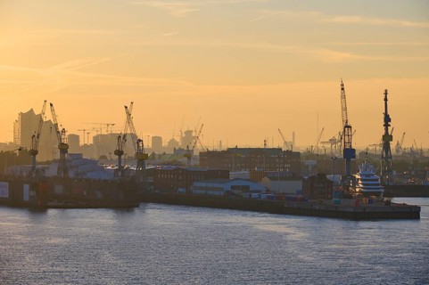 Harbour at sunrise, cranes rise into the sky, in the background buildings, Elbe Philharmonic Hall,