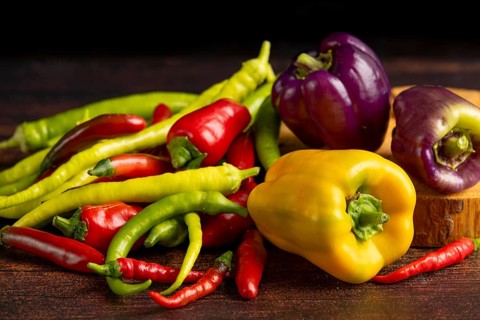 Colourful peppers and chillies arranged on a dark wooden surface, food photography