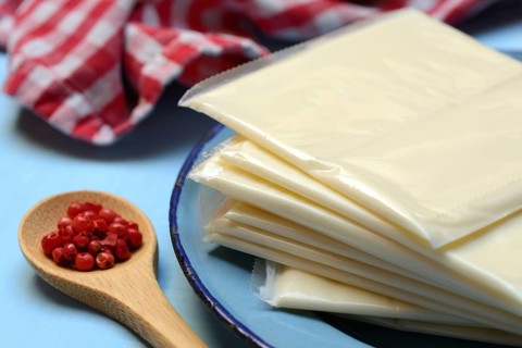 Processed cheese, slices of processed cheese wrapped in plastic and spoon with pink berries, red