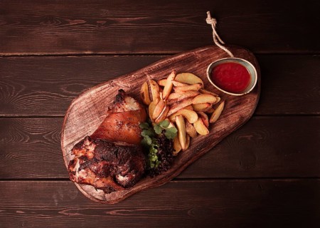 Pork knuckle, in soy-honey sauce, with fried potatoes, on a wooden chopping board, homemade, no
