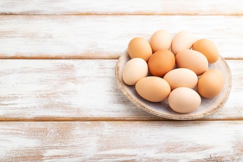Pile of colored chicken eggs on plate on a white wooden background. side view, copy space, close up