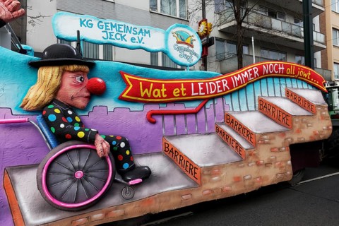 Wheelchair user in jester's costume waiting in front of steps, papier-mâché figure, motif float on