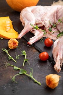 Whole raw rabbit with pumpkin, tomatoes, pea sprouts on a black concrete background and linen