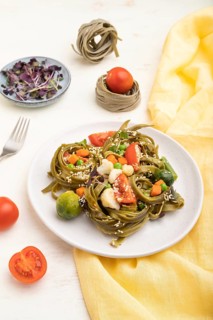Tagliatelle green spinach pasta with tomato, pea and microgreen sprouts on a white wooden